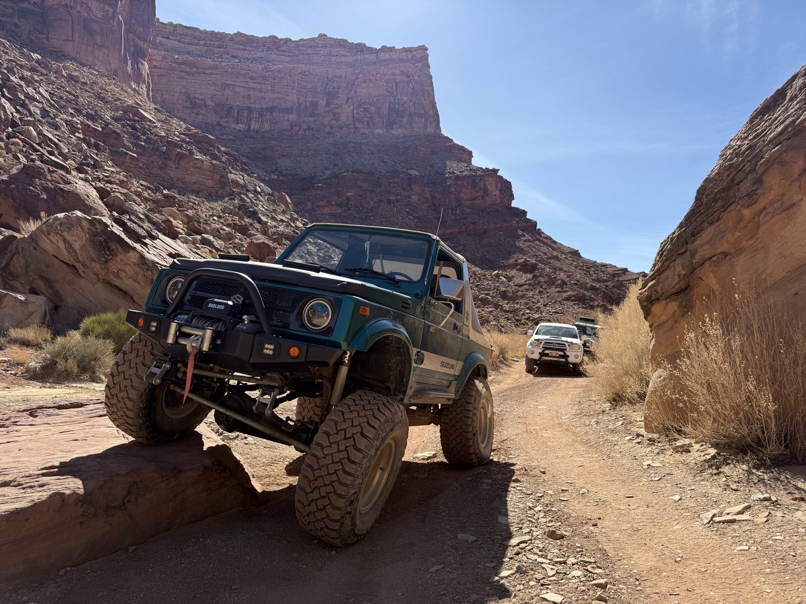 Vehicle on a narrow desert road below canyon cliffs